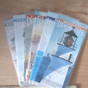 May include: A collection of lighthouse maps, each in a clear plastic sleeve. The maps feature illustrations of lighthouses and coastal scenes. The title "Massachusetts Lighthouses" is visible on one map. The maps are from Bartlett House Map Publisher.