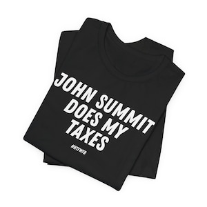 May include: A black t-shirt featuring the white text JOHN SUMMIT DOES MY TAXES in a bold, sans-serif font, with the hashtag #HTFWFB printed in a smaller white font directly underneath the main text on the front of the folded garment.