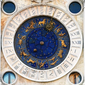 May include: A detailed close-up of an ornate clock face. The clock features a blue center with gold zodiac symbols and a sun. Roman numerals mark the hours on a white outer ring. The clock is set in a stone wall.