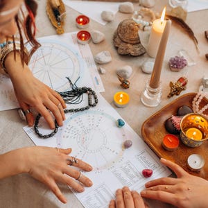 May include: A table setting for a spiritual reading, featuring astrological charts, candles, crystals, and beads. The scene includes lit candles, gemstones, and a wooden tray, creating a mystical atmosphere.