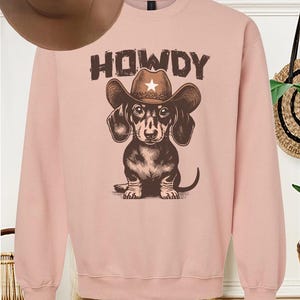 May include: A pink sweatshirt with a brown dachshund wearing a cowboy hat and the word "HOWDY" printed on it.
