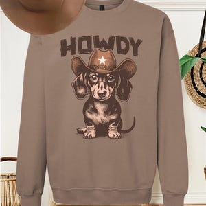 May include: A brown sweatshirt with a dachshund wearing a cowboy hat and the word "HOWDY" printed on it.