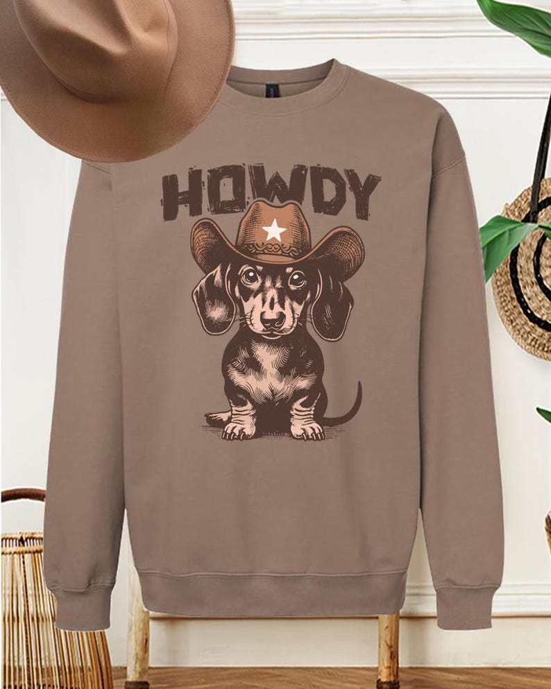 May include: A brown sweatshirt with a dachshund wearing a cowboy hat and the word "HOWDY" printed on it.