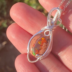 May include: A silver wire wrapped pendant featuring a teardrop-shaped opal with orange, green, and red iridescent flashes. The pendant is attached to a silver chain.