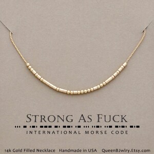 A gold filled necklace with a chain and beads that spell out the words 'STRONG AS FUCK' in morse code. '14k Gold Filled Necklace Handmade in USA QueenBJwlry.Etsy.com' is at the bottom of the image.