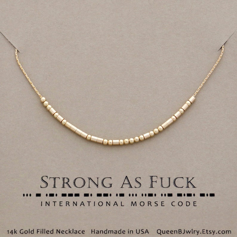 A gold filled necklace with a chain and beads that spell out the words 'STRONG AS FUCK' in morse code. '14k Gold Filled Necklace Handmade in USA QueenBJwlry.Etsy.com' is at the bottom of the image.