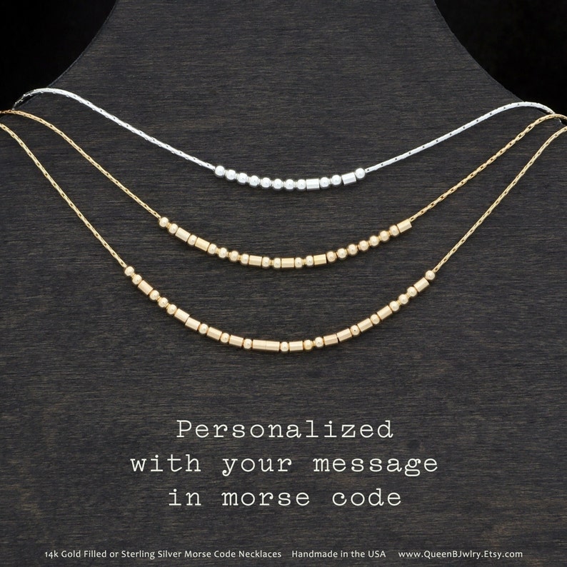 Three gold filled or sterling silver morse code necklaces on a black background. The necklaces are layered on top of each other. The text reads 'Personalized with your message in morse code' and '14k Gold Filled or Sterling Silver Morse Code Necklaces Handmade in the USA www.QueenBJwlry.Etsy.com'.