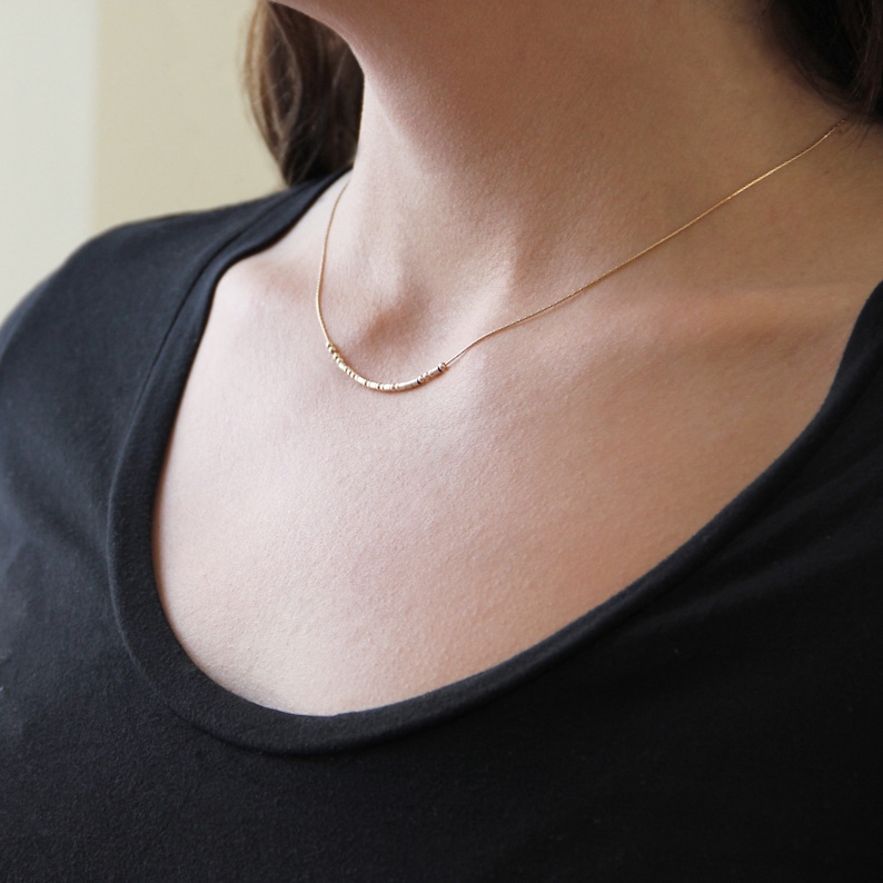 Delicate, dainty 14k gold filled morse code necklace on the neck of a model.
