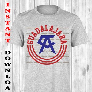 May include: A heather gray t-shirt featuring a Guadalajara design. The design includes the word "Guadalajara" in red, a blue and white emblem, and red concentric circles. The shirt also has the words "Instant Download" in black.
