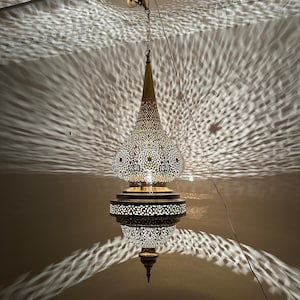 May include: A gold metal pendant light fixture with a geometric pattern. The light fixture is hanging from a chain and has a teardrop shape.