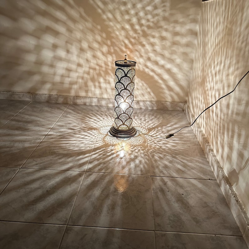 May include: A tall, silver floor lamp with a decorative, patterned metal shade. The lamp casts intricate shadows on the tiled floor.