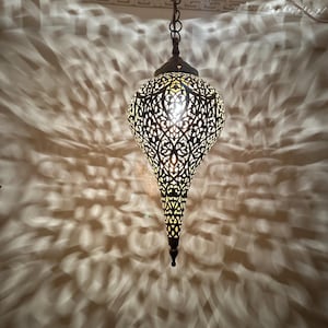 May include: A gold-toned metal pendant light with intricate cut-out designs. The light is hanging from a chain and casts a patterned shadow on the ceiling.