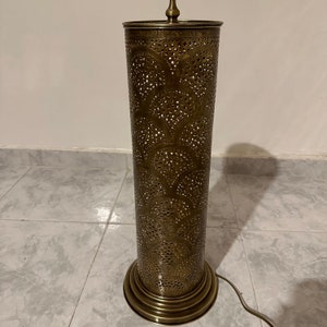 May include: A tall, gold-colored metal floor lamp with a cylindrical shade featuring a decorative, intricate cut-out pattern.