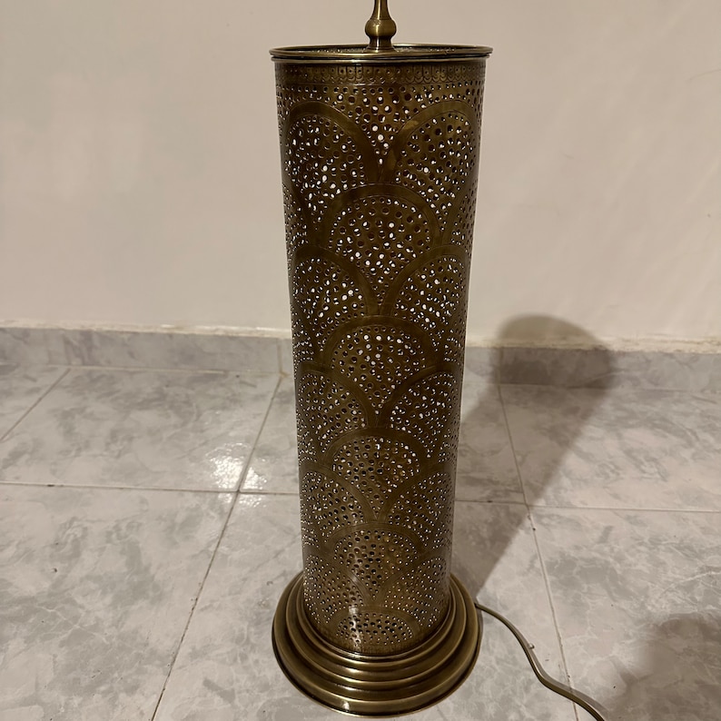May include: A tall, gold-colored metal floor lamp with a cylindrical shade featuring a decorative, intricate cut-out pattern.