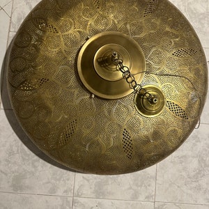 May include: A round, brass ceiling light fixture with a decorative, cut-out pattern. The light has a chain and a small, round, brass cap.