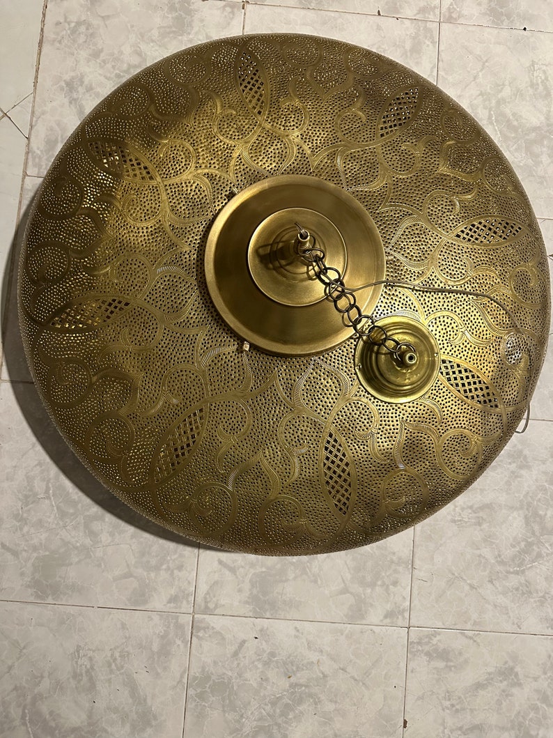May include: A round, brass ceiling light fixture with a decorative, cut-out pattern. The light has a chain and a small, round, brass cap.
