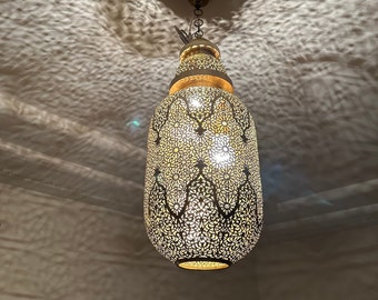 Puede incluir: Una lámpara colgante de metal dorado con un diseño decorativo, intrincado y recortado. La lámpara está colgada de una cadena.