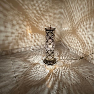 May include: A tall, decorative floor lamp with a metal, geometric design. The lamp casts intricate shadows on the tiled floor.