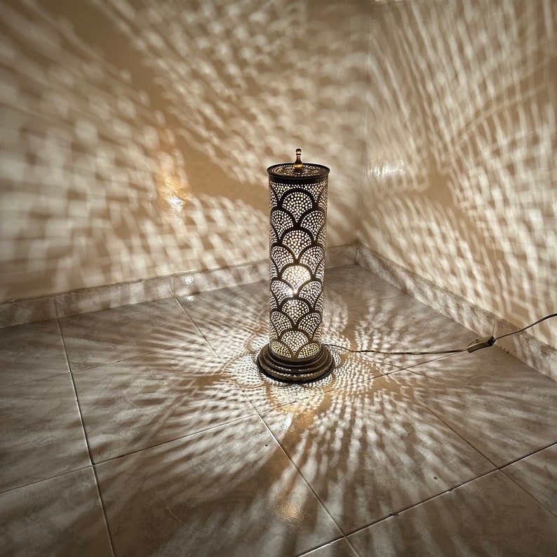 May include: A tall, decorative floor lamp with a metal, geometric design. The lamp casts intricate shadows on the tiled floor.