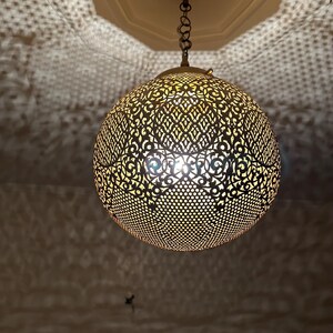 May include: A round, gold-colored metal pendant light fixture with intricate cut-out designs. The light fixture is hanging from a chain.