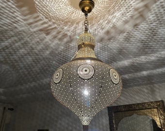 Puede incluir: Una lámpara colgante de metal dorado con un diseño redondo y ornamentado. La lámpara está colgada del techo y proyecta un patrón de luz en la pared.