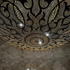 May include: A black metal ceiling light fixture with a round, ornate design. The light fixture has a pattern of small holes that allow light to shine through, creating a decorative effect.