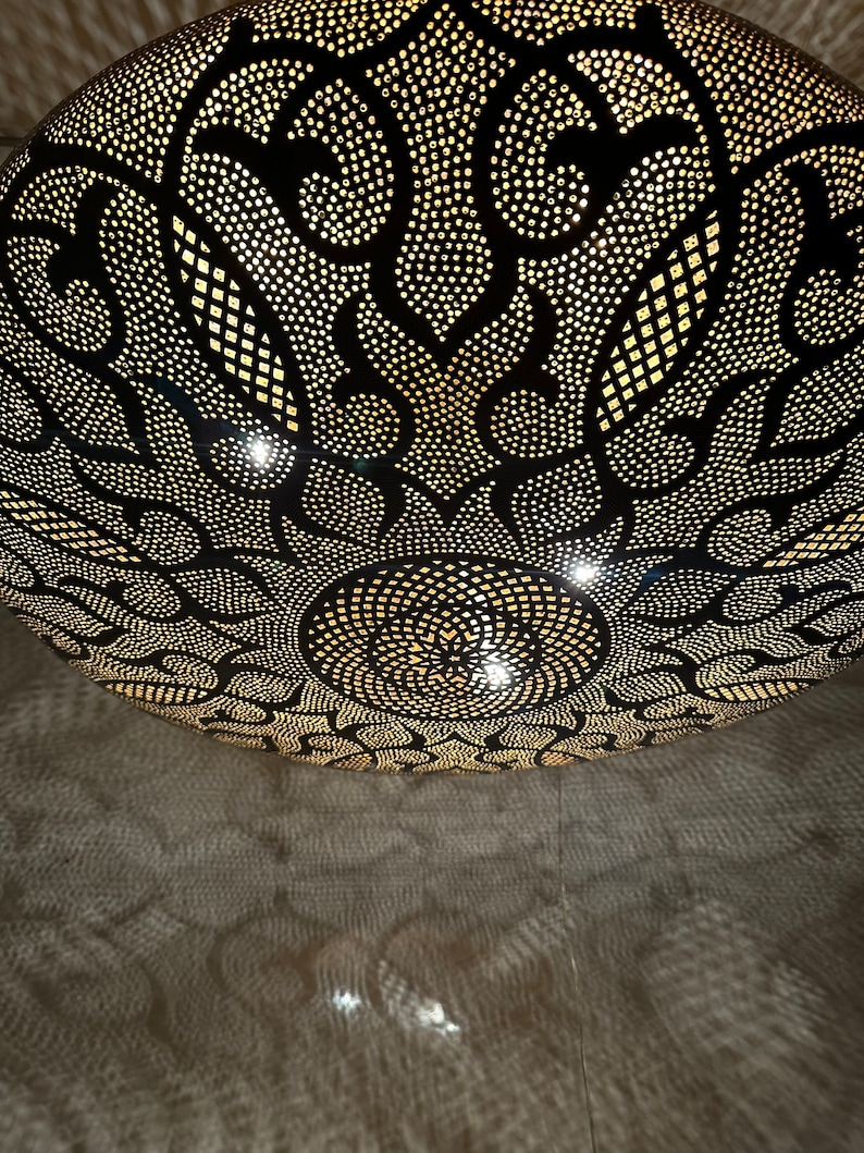May include: A black metal ceiling light fixture with a round, ornate design. The light fixture has a pattern of small holes that allow light to shine through, creating a decorative effect.