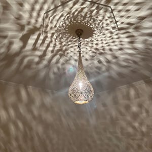 May include: A decorative, teardrop-shaped pendant light fixture with intricate cut-out patterns. The light casts a complex shadow pattern on the ceiling. The fixture is suspended from a chain and has a warm, inviting glow.