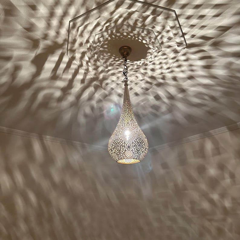 May include: A decorative, teardrop-shaped pendant light fixture with intricate cut-out patterns. The light casts a complex shadow pattern on the ceiling. The fixture is suspended from a chain and has a warm, inviting glow.