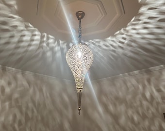Puede incluir: Una lámpara colgante decorativa de metal con una pantalla perforada en forma de lágrima. La luz proyecta intrincados patrones en el techo.