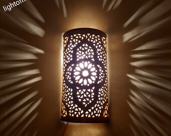 May include: A white Moroccan-style wall sconce with intricate geometric cutouts. The light is on, casting a warm glow through the design.