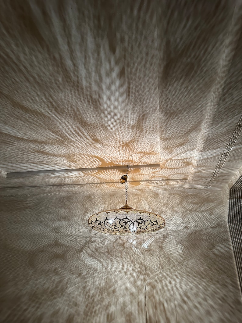 May include: A gold-toned metal pendant light fixture with a round, openwork design casts intricate shadows on the ceiling. The light fixture has a chain and a decorative finial.