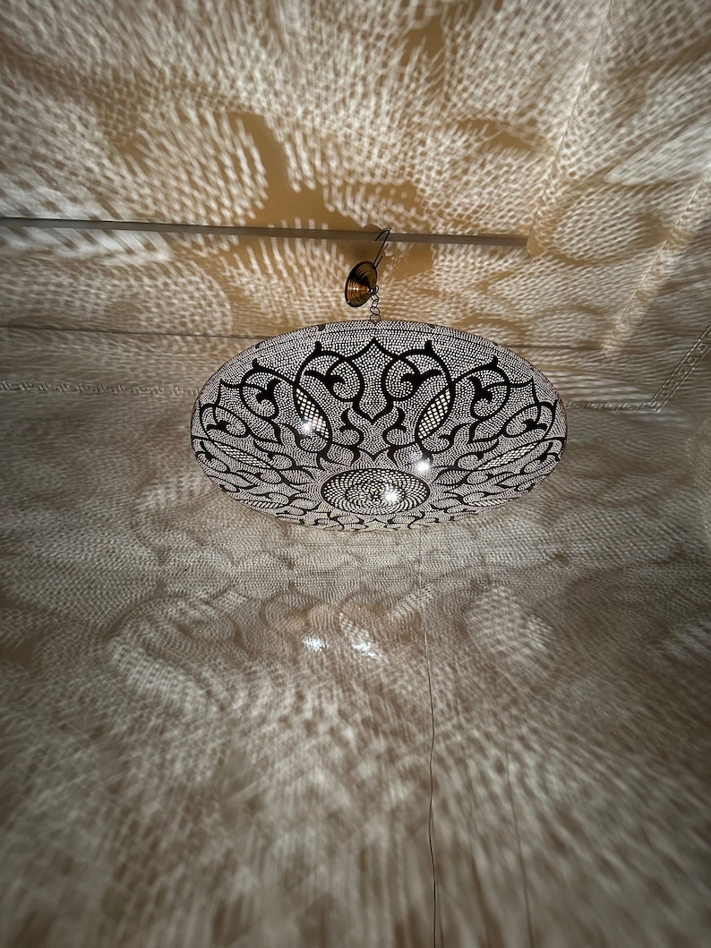 May include: A round, black metal ceiling light fixture with intricate cut-out designs. The light casts a patterned shadow on the ceiling.