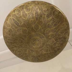May include: A round, brass ceiling light fixture with a decorative, intricate, cut-out pattern. The light fixture is gold in color and has a circular shape.