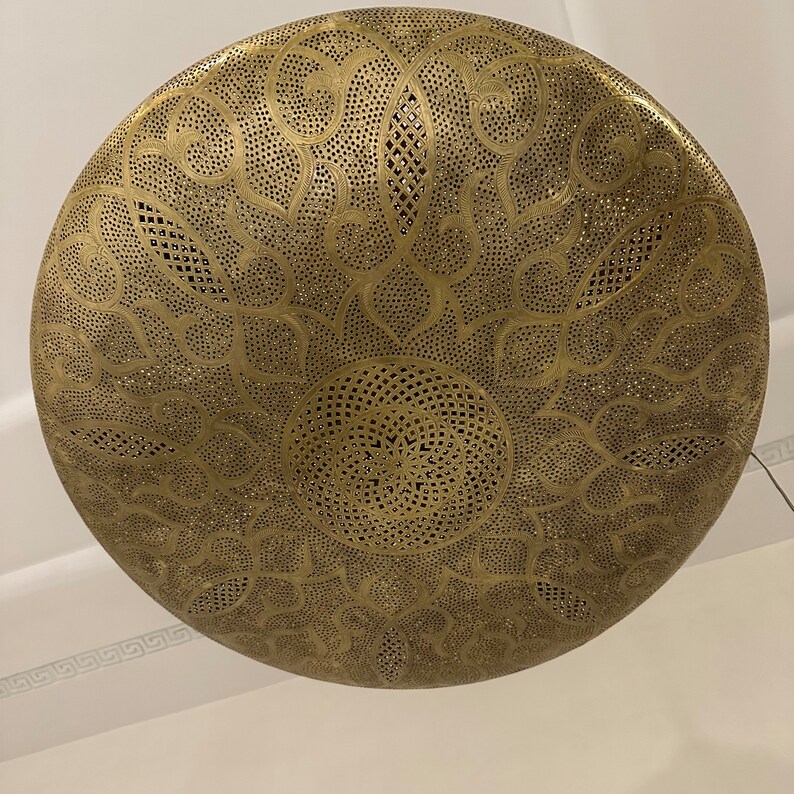 May include: A round, brass ceiling light fixture with a decorative, intricate, cut-out pattern. The light fixture is gold in color and has a circular shape.