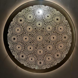 May include: A round, decorative ceiling light fixture with a intricate, geometric pattern of cut-outs. The light shines through the cut-outs, creating a beautiful pattern on the ceiling.