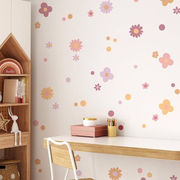 Puede incluir: Una pared blanca con calcomanías de flores rosas y naranjas y pequeños círculos. La pared está decorada con un escritorio, una silla y una estantería. La estantería tiene un arcoíris y la palabra "hello" en ella.