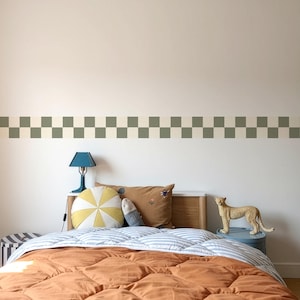 Può includere: Interno di una camera da letto con un letto coperto da un piumino arancione e lenzuola a righe blu e bianche. Cuscini decorativi e una lampada blu sono sulla testiera in legno. Un bordo a scacchi verde e crema adorna il muro.