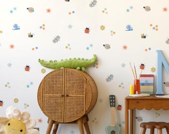 May include: A white wall with colorful insect and flower decals. A wicker cabinet with two doors sits in front of the wall. A stuffed crocodile sits on top of the cabinet. A guitar leans against the wall. A small wooden table with a stool sits in the corner of the room.