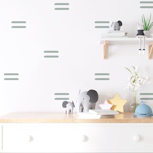 Puede incluir: Una cómoda blanca con dos cajones y una tapa de madera clara. La cómoda está decorada con pegatinas de pared grises de doble línea. Hay dos figuritas de elefante grises, una estrella rosa y amarilla y una figurita de ballena azul en la parte superior de la cómoda.