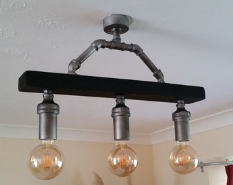 May include: A black wooden ceiling light fixture with three Edison bulbs. The fixture is made of industrial pipes and has a rustic look.