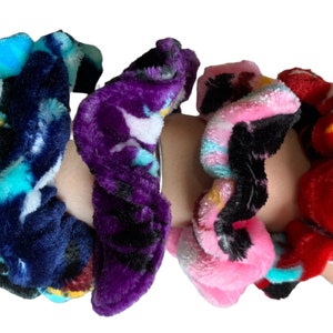 May include: Four colorful scrunchies with a variety of patterns. The scrunchies are made of a soft, fuzzy fabric and are perfect for holding hair in place.