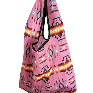 May include: Pink reusable shopping bag with a Southwestern geometric pattern in black, turquoise, orange, and white. The bag has a black trim and a handle for carrying. The bag is made of a lightweight, foldable material.