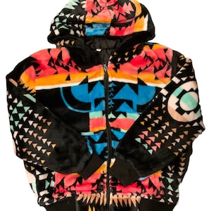 Könnte beinhalten: Eine schwarze Kapuzenjacke mit einem bunten geometrischen Muster. Das Muster zeigt Farbtöne von Rosa, Blau, Gelb und Grün. Die Jacke hat einen Reißverschluss und einen schwarzen gerippten Bund.