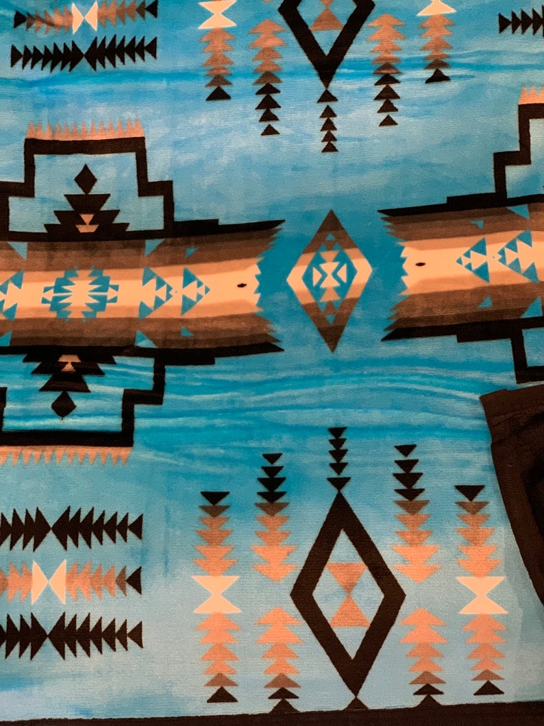 May include: A blue and black patterned throw blanket with a geometric design. The blanket features a diamond shape in the center with a smaller diamond inside. The blanket is made of a soft, plush material.