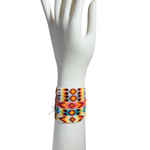 Könnte beinhalten: Ein Set aus vier Perlenarmbändern mit einem geometrischen Muster in den Farben Weiß, Orange, Gelb, Blau und Rosa.