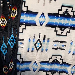 May include: A close-up of two blankets with geometric patterns. One blanket is black with colorful diamond and triangle designs. The other blanket is white with blue and black geometric shapes. The blankets have a soft, textured appearance.