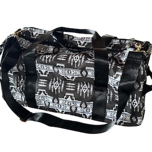 Könnte beinhalten: Eine schwarz-weiß gemusterte Reisetasche mit geometrischem Design. Die Tasche hat schwarze Griffe und einen Schultergurt. Die Tasche ist für Reisen konzipiert und hat eine rechteckige Form.