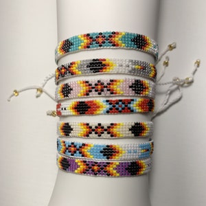 May include: A stack of six colorful beaded bracelets with geometric patterns. The bracelets are made with white, black, red, yellow, blue, and purple beads.