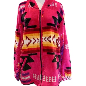 Può includere: Una felpa con cappuccio con zip rosa in pile con un motivo geometrico in nero, bianco, rosso, giallo e viola. La felpa ha un cappuccio e una tasca anteriore.